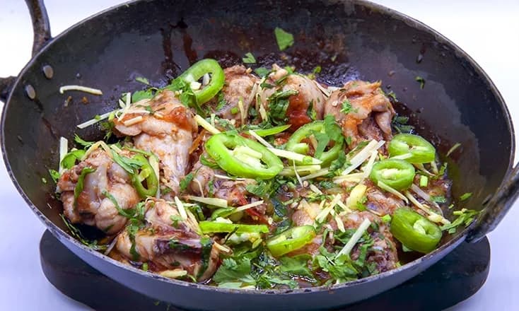 Chicken Karahi in a black karahi with green chilli, ginger and coriander
