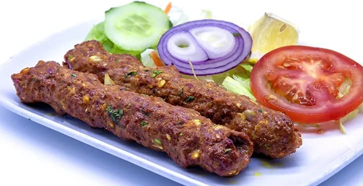 Three grilled kebabs served with cucumber, red onion, tomato and lemon
